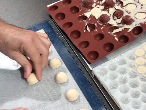 Des demi sphères de pâte à choux sont posées sur une plaque de cuisson perforée recouverte d'un tapis de cuisson en silicone