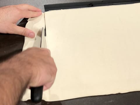 L'excédent de pâte feuilletée qui dépasse de la plaque de cuisson, est coupé avec un couteau