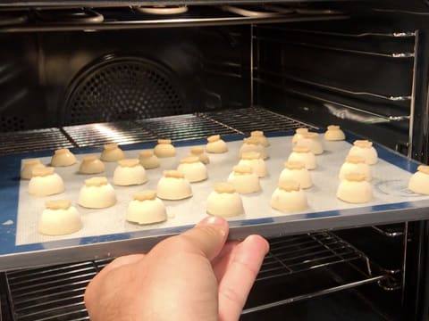 La plaque de cuisson perforée recouverte d'un tapis de cuisson en silicone sur lequel se trouvent les choux recouverts de craquelin, est placée dans le four