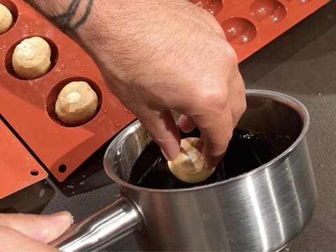 Un gros chou est trempé dans le caramel liquide qui se trouve dans la casserole