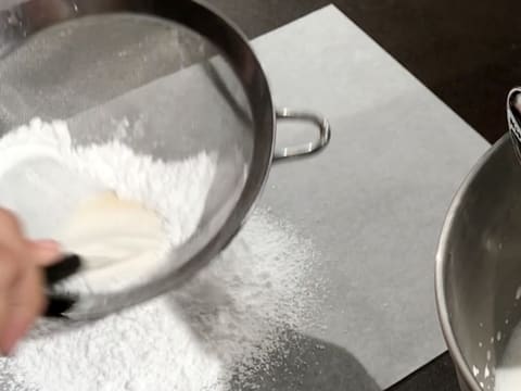 Le sucre glace est tamisé dans une passoire fine au-dessus d'une feuille de papier sulfurisé