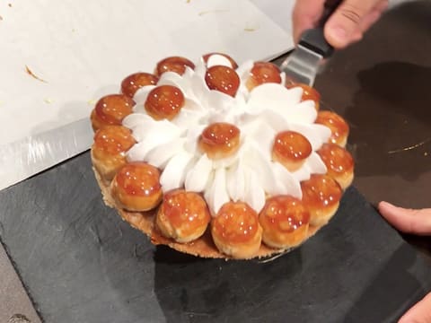 Obtention du gâteau Saint-Honoré qui est placé sur un plat en ardoise, à l'aide d'une spatule métallique coudée