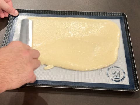 La pâte à biscuit est étalée sur toute la surface du tapis silicone à l'aide d'une spatule métallique coudée