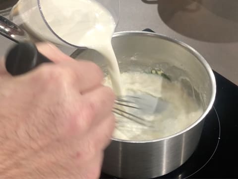 Le lait est versé sur le roux blanc dans la casserole, tout en étant mélangé au fouet