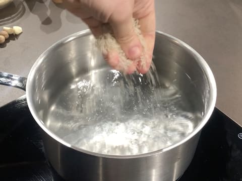 Du gros sel est versé dans une casserole remplie d'eau qui est posée sur une plaque de cuisson