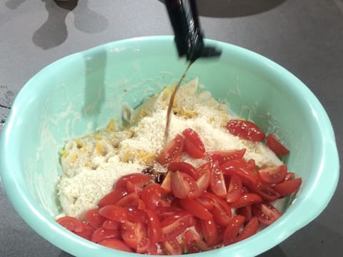 Ajout de la sauce Worcester sur les quartiers de tomates cerises, les fromages râpés et les pâtes cuites et enrobées de sauce béchamel qui se trouvent dans le cul de poule posé sur le plan de travail