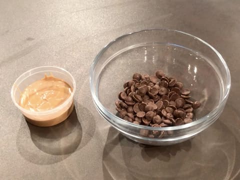 Un petit récipient contenant du praliné amandes noisettes et un grand bol en verre contenant des pistoles de chocolat au lait sont placés sur le plan de travail