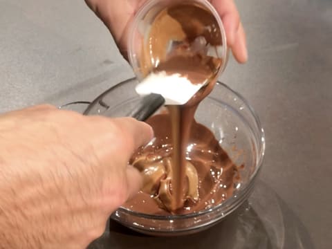 Le praliné amandes noisettes est versé sur le chocolat au lait fondu dans le grand bol en verre