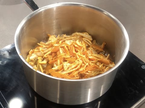 Les fines lanières d'écorce sont placées sur les segments des clémentines, dans la casserole qui est posée sur la plaque de cuisson