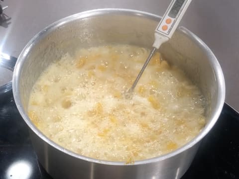 Prise de la température de la préparation à base de lanières d'écorce et de segments de clémentines en ébullition dans la casserole, avec le thermomètre de cuisine qui affiche 104°C