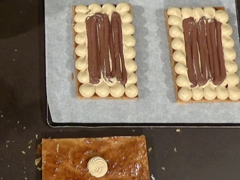 Obtention de deux plaques de pâte feuilletée recouvertes de mousseline café et de crémeux chocolat, et d'une plaque de pâte feuilletée ornée d'une rosace de crème mousseline café