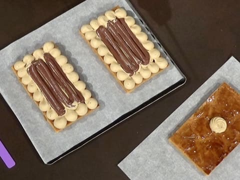 Les deux plaques de pâte feuilletée recouvertes de mousseline café et de crémeux chocolat, et la plaque de pâte feuilletée ornée d'une rosace de crème mousseline café sont refroidies et placées sur le plan de travail