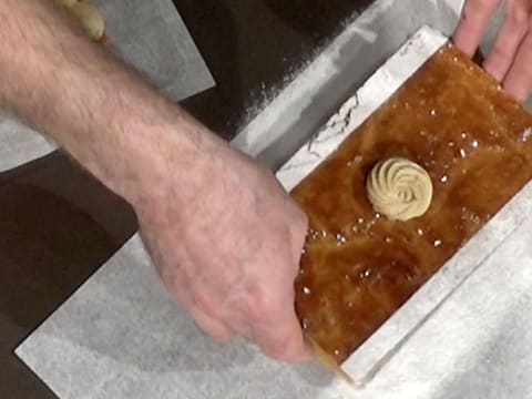 La plaque de pâte feuilletée ornée d'une rosace de crème mousseline café est soulevée avec les deux mains