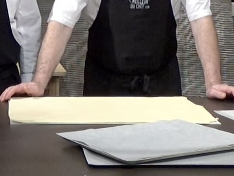 Vision de la pâte feuilletée positionnée à l'horizontale sur le plan de travail, et de deux plaques à pâtisserie recouvertes de papier sulfurisé