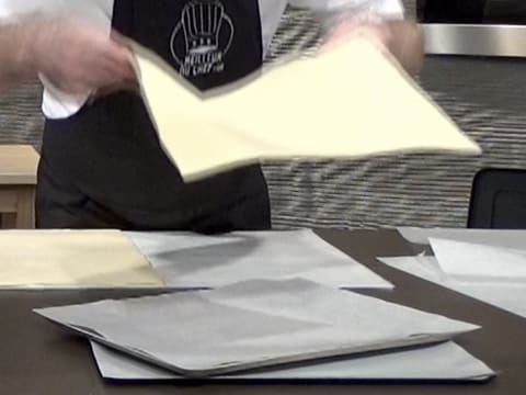 Une des moitiés de pâte feuilletée est prise à deux mains pour être placée sur une plaque à pâtisserie recouverte de papier sulfurisé