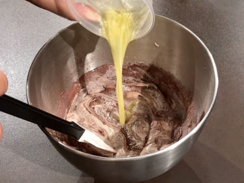 Ajout du beurre fondu dans la préparation chocolatée dans la cuve du batteur, et mélange avec la spatule maryse