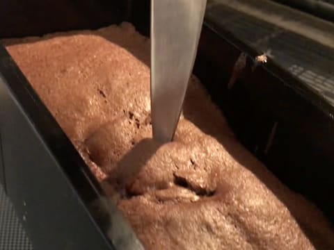 La lame d'un couteau est plantée dans la génoise au chocolat qui est cuite dans son moule à pain de mie