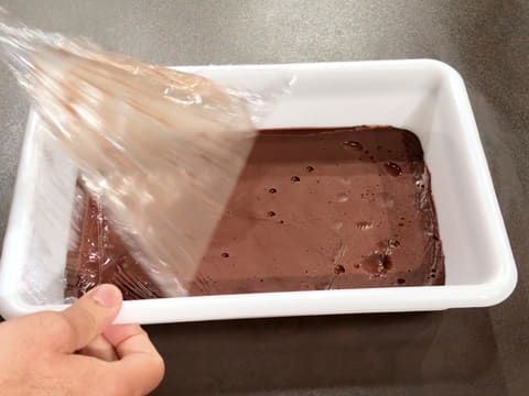 La feuille de papier film est retirée de la ganache au chocolat qui dans un bac alimentaire