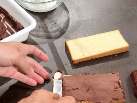 La ganache au chocolat est étalée sur la première tranche de génoise vanillée avec une spatule métallique