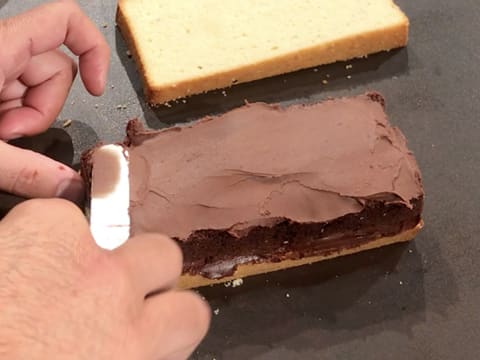 À l'aide d'une spatule métallique coudée, la ganache au chocolat est étalée de manière régulière sur toute la surface de la génoise au chocolat