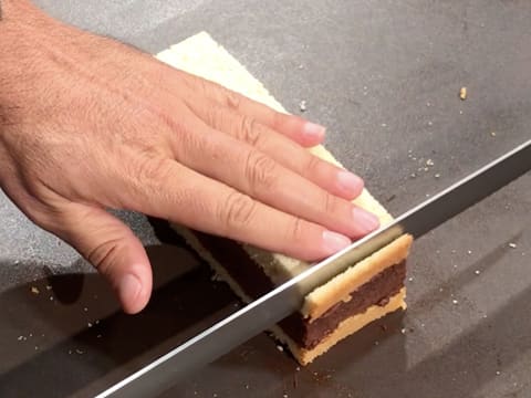 Un bout de l'entremets est paré à l'aide du couteau-scie à génoise