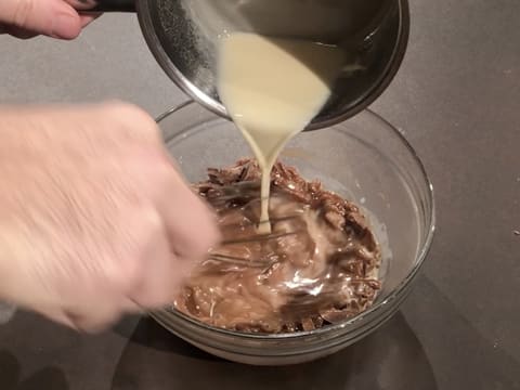 Ajout d'un peu de mélange de lait concentré et de sirop de glucose sur le chocolat haché dans le saladier en verre