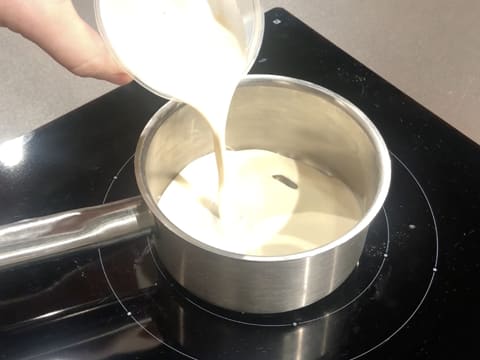 Ajout du lait concentré non sucré sur le sirop de glucose dans la casserole qui est posée sur la plaque de cuisson