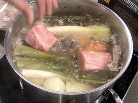 Ajout des os à moelle dans l'eau frémissante dans le grand faitout qui contient tous les ingrédients pour le pot au feu