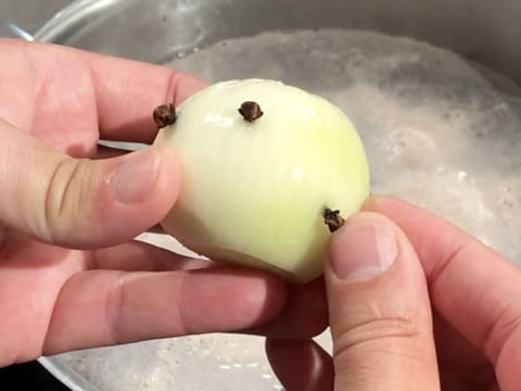 Trois clous de girofle sont piqués dans un oignon épluché