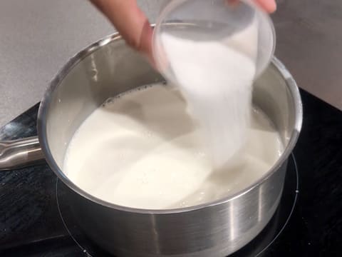 Ajout du sucre en poudre dans le lait qui est en train de cuire dans une casserole