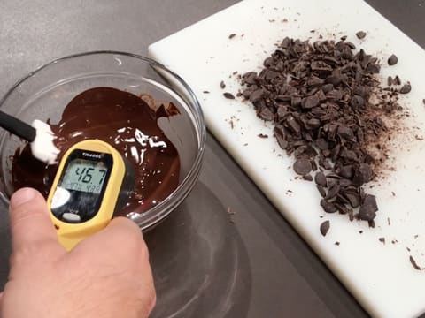Prise de la température d'un bol de chocolat noir fondu, et chocolat noir haché sur une planche à découper
