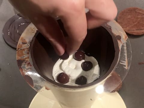 Six cerises à l'eau de vie sont piquées dans la Chantilly dans le cône en chocolat