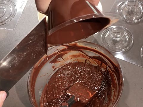 L'excédent de chocolat s'écoule du moule en tapotant ce dernier avec une spatule