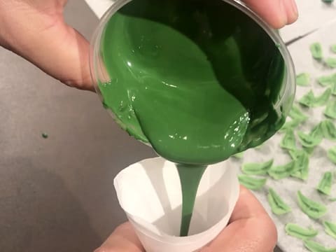 Un peu de chocolat vert fondu est versé dans un cornet décor en papier sulfurisé
