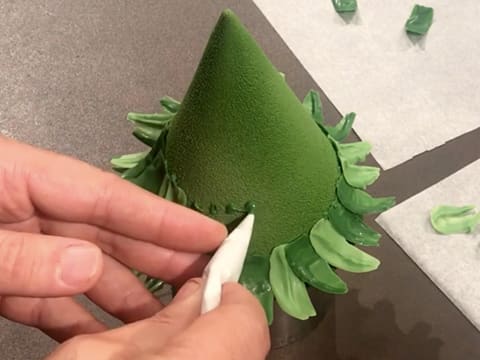 Des gouttes de chocolat vert sont déposées sur un deuxième étage du sapin en chocolat vert