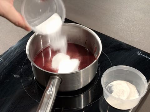 Ajout du sucre en poudre dans une casserole contenant la purée de griotte