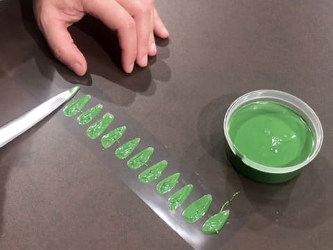 La pointe de la lame du couteau contenant du chocolat vert, est posée sur une bande de ruban pvc pour réaliser des feuilles