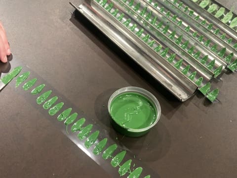 Une plaque à tuiles est remplie de bandes de ruban pvc sur lesquelles des feuilles de chocolat vert ont été posées