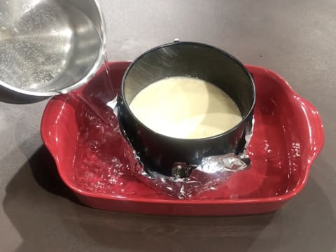 Un peu d'eau est versée dans le plat à gratin qui contient le moule à charnière dans lequel se trouve l'appareil au fromage blanc