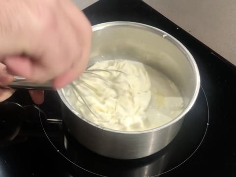 Mélange au fouet de la préparation à base de fromage blanc dans la casserole qui se trouve sur la plaque de cuisson