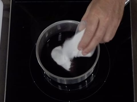 Le sucre en poudre est versé dans une casserole qui contient de la purée de myrtille