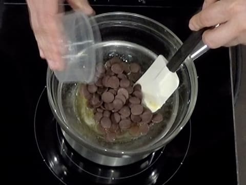 Les pistoles de chocolat au lait sont versées dans le beurre de cacao Mycryo fondu et le tout est mélangé à la spatule maryse dans le saladier qui est placé sur un bain-marie