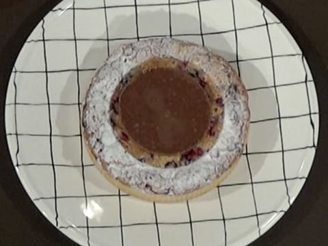 La tarte de fruits rouges qui est sur son plat de service, est décorée au centre avec le disque de croustillant praliné et décorée de sucre glace sur tout le pourtour