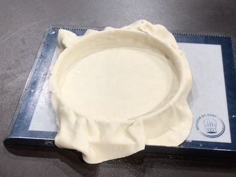 Le cercle à tarte qui est posé sur la plaque à pâtisserie recouverte d'une toile en silicone, est foncé avec la pâte feuilletée