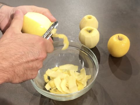 Une pomme est épluchée au dessus d'un saladier en verre à l'aide d'un éplucheur