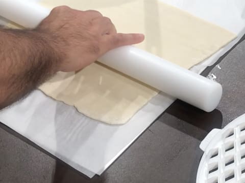 La pâte feuilletée est abaissée au rouleau à pâtisserie sur le plan de travail recouvert d'une feuille de papier sulfurisé