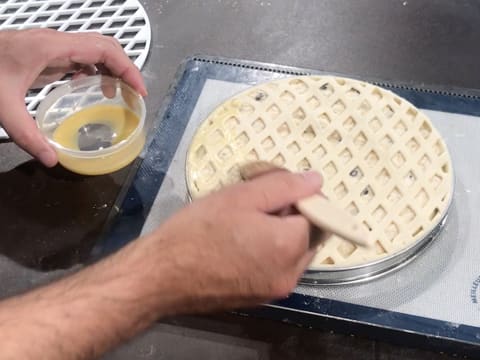 La surface du décor en pâte feuilletée grillagée est dorée à l'aide du pinceau pâtissier