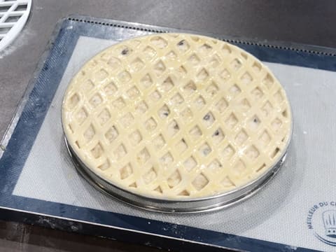 Obtention de la tarte normande crue dont la surface est dorée avec une dorure, et qui est placée sur une plaque à pâtisserie recouverte d'un tapis de cuisson en silicone