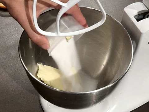 Ajout du sucre en poudre sur le beurre pommade dans la cuve du batteur muni de l'accessoire feuille