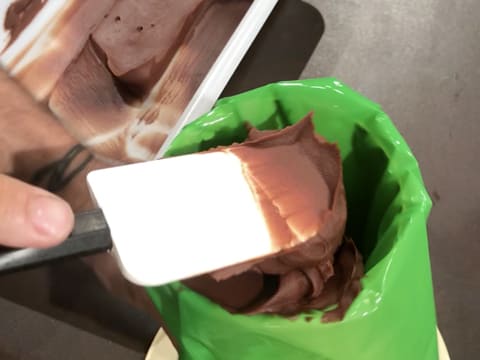 La ganache au chocolat est versée dans la poche à douille avec la spatule maryse